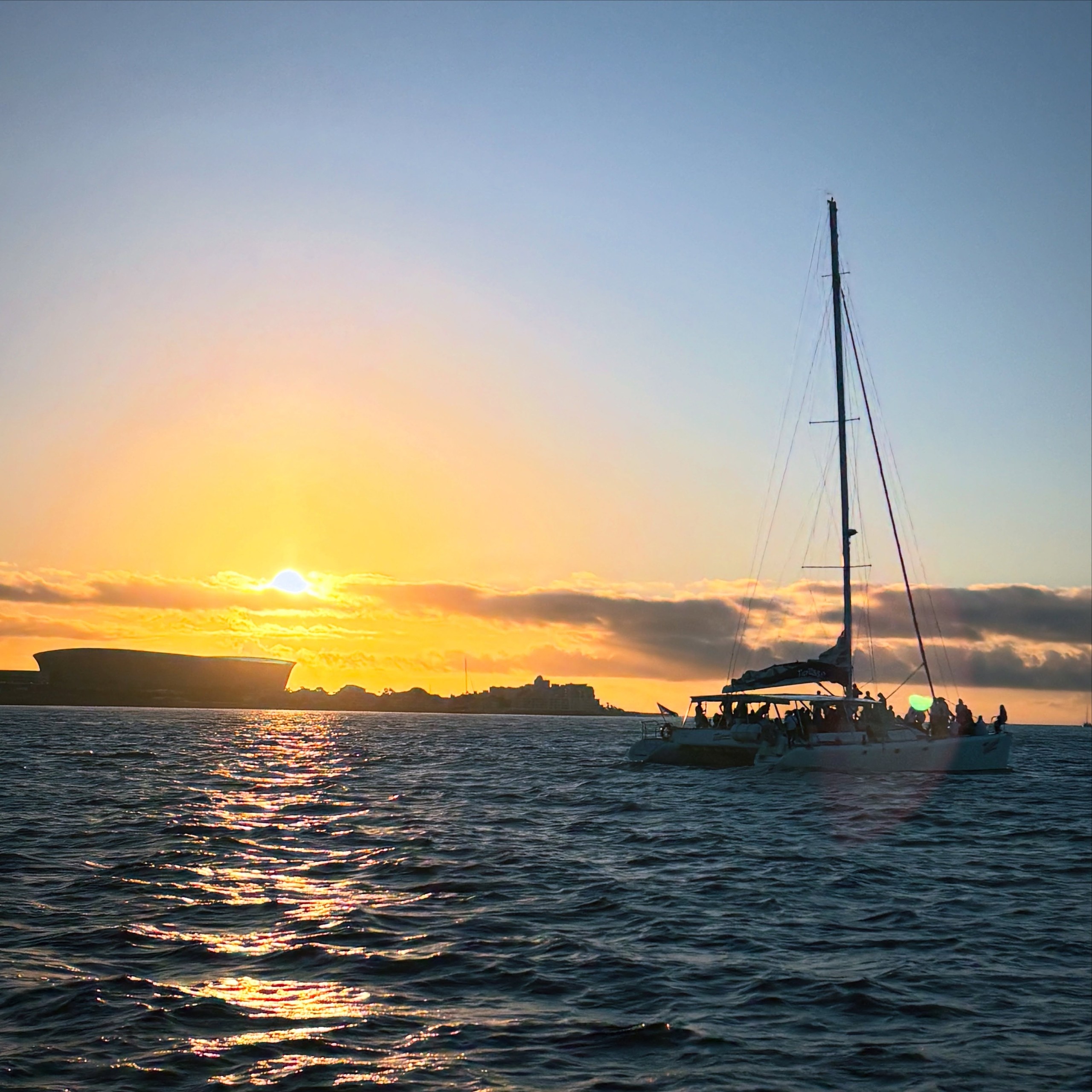 Sailboat on water during sunset with building in background.