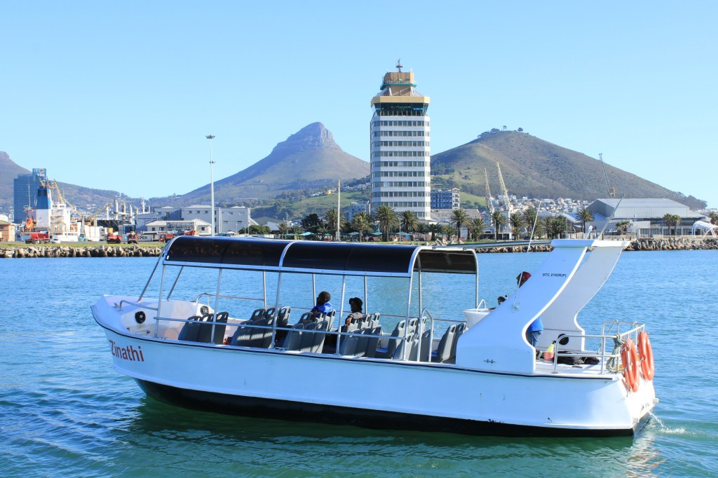 White boat on water with mountains and tower in background under clear blue sky.