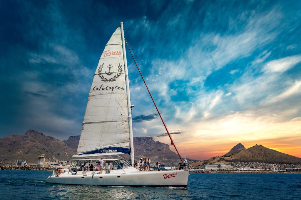 Sailboat on water with people, mountains, and dramatic sky at sunset.