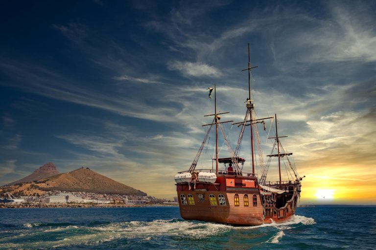 Sailing ship on the ocean near a mountain at sunset.