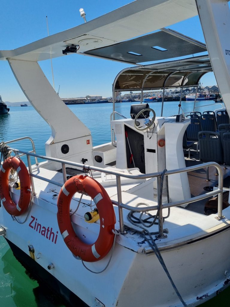 Small white boat with life rings and blue seats docked in a harbor.