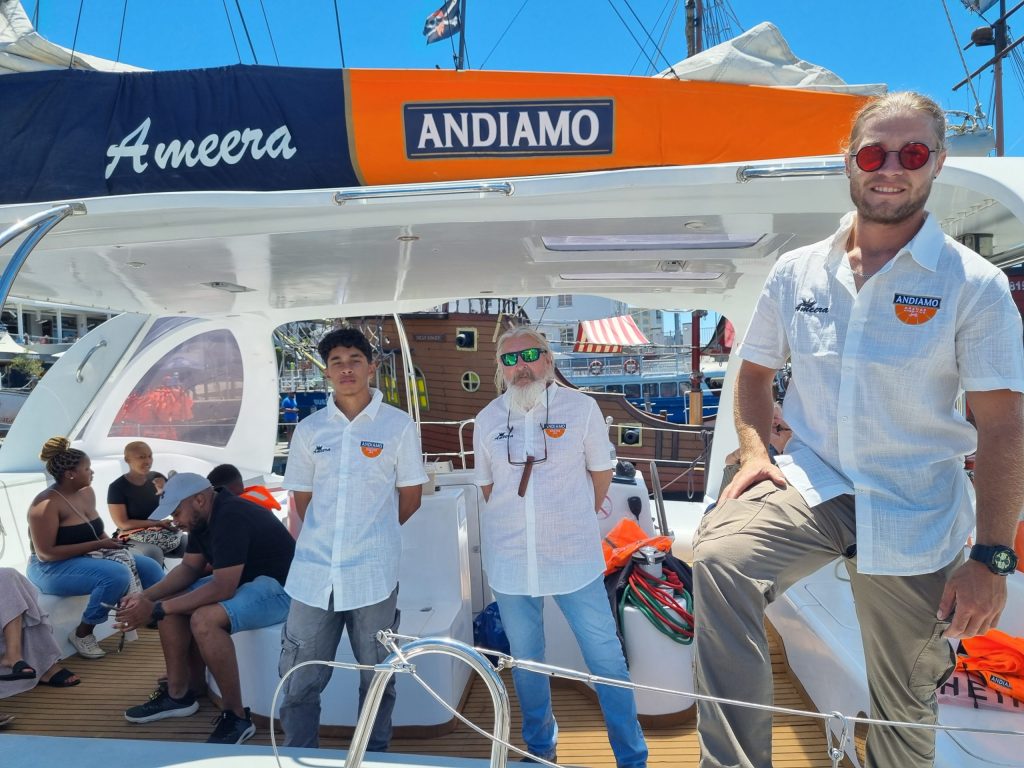 Three men in matching shirts on a boat with seated passengers, under a bright sky.
