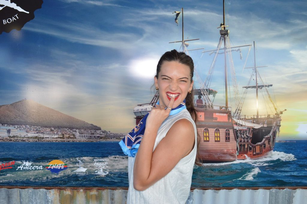 Woman smiling in front of a mural showing a ship at sea.