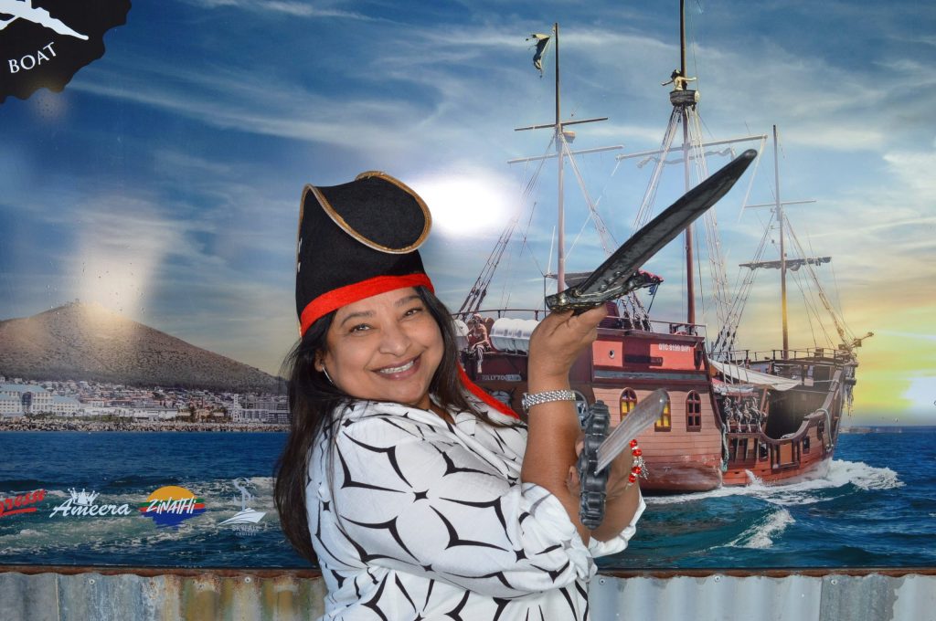 Smiling woman in pirate hat poses with sword in front of ship mural.