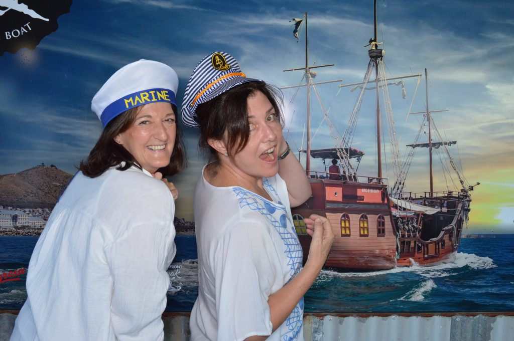 Two people in sailor hats posing in front of ship mural.