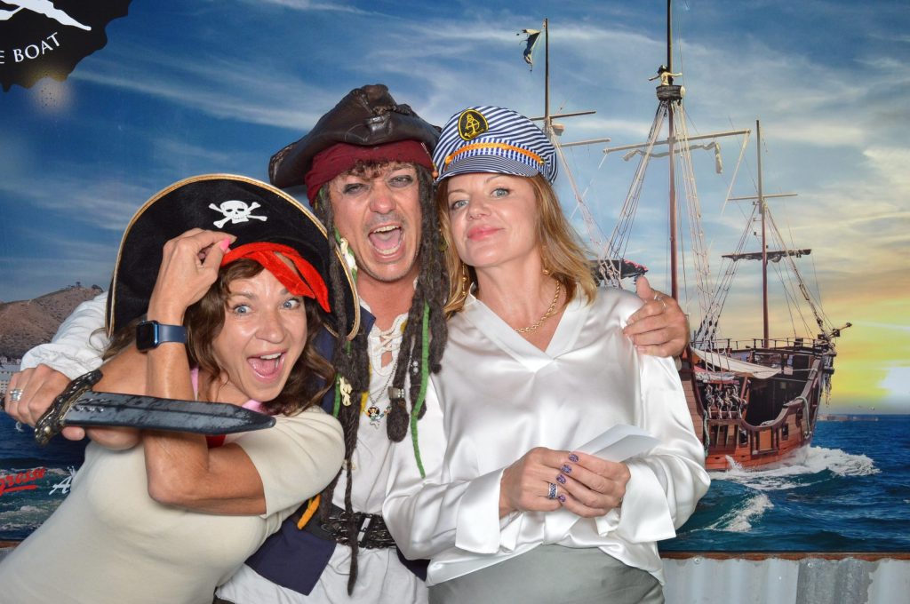 Three people in pirate costumes posing with a ship backdrop.