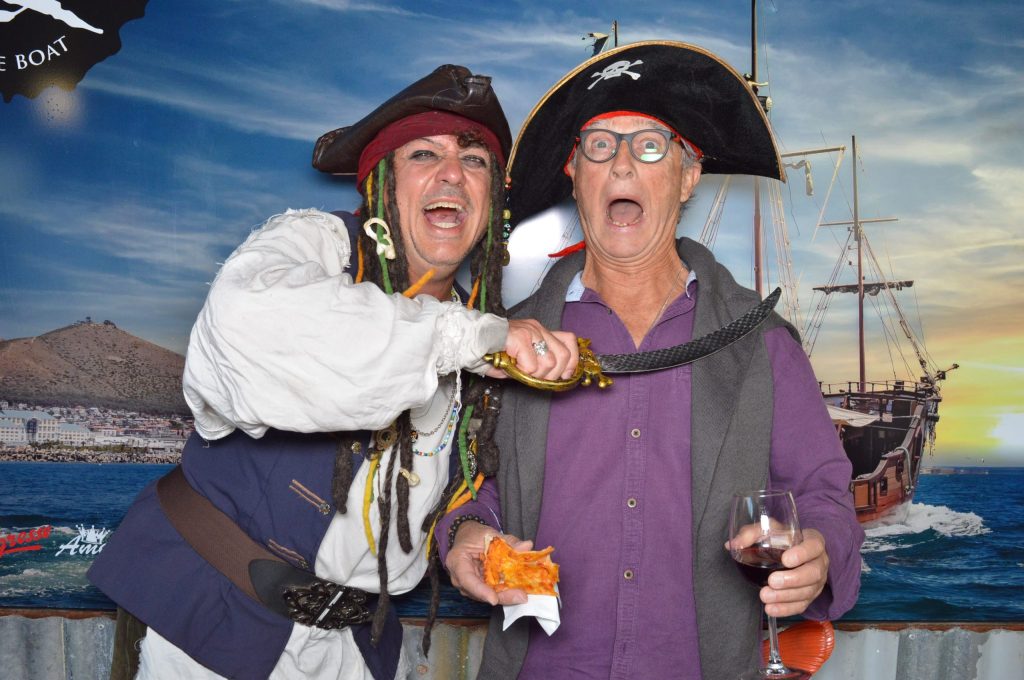 Two people in pirate costumes posing playfully with a backdrop of a pirate ship.