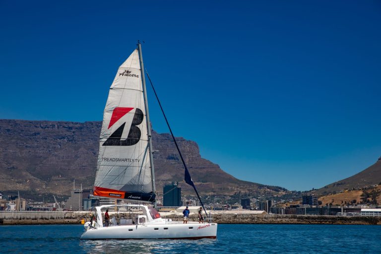 Sailboat with large sail in front of mountainous coastline on a clear day.