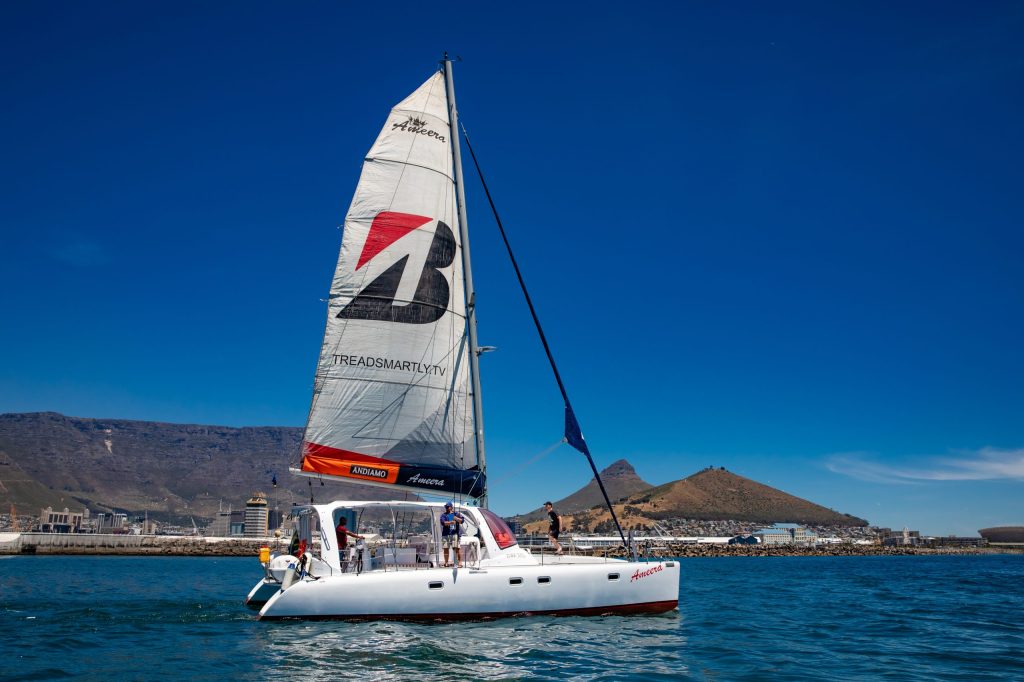 White sailboat on calm water with hills in the background under a clear blue sky.