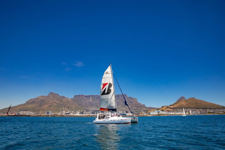 Sailboat on the ocean with mountains and clear blue sky in the background.