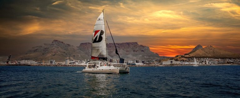 Sailboat on ocean at sunset with mountains in background.