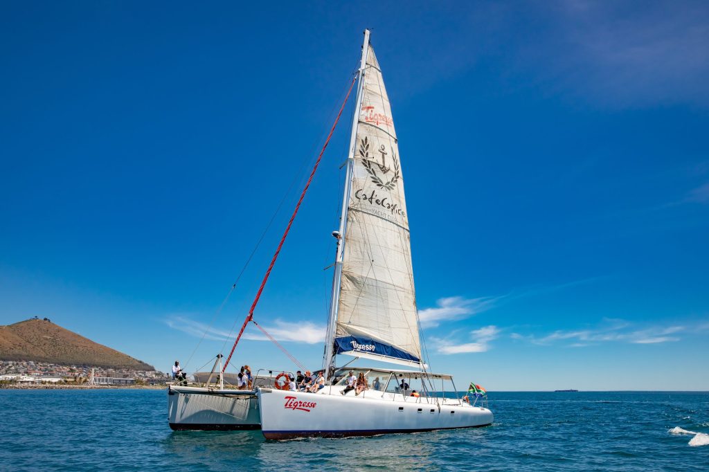 White sailboat with people sailing on a clear blue ocean under a bright sky.