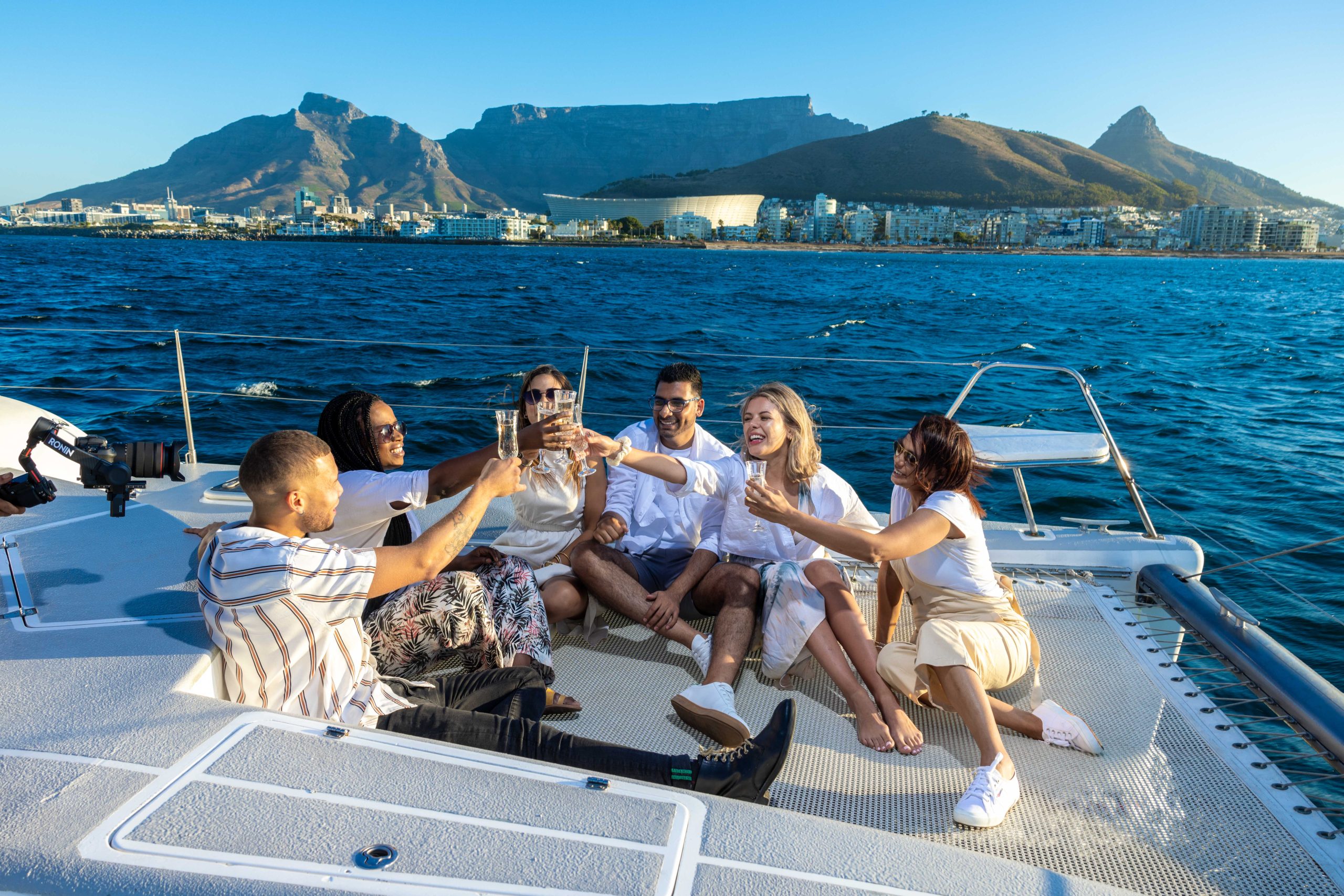 Group of six people toasting on a boat with a mountain and city in the background.
