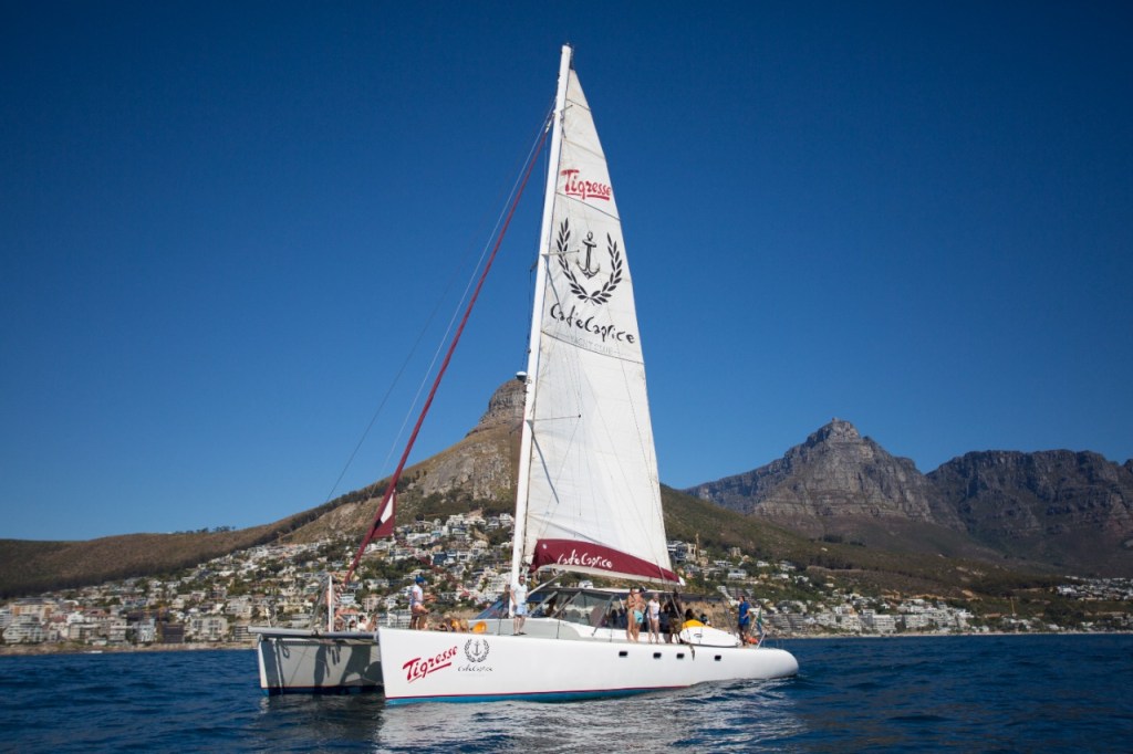 A white sailboat on the sea, with mountains and a city in the background.