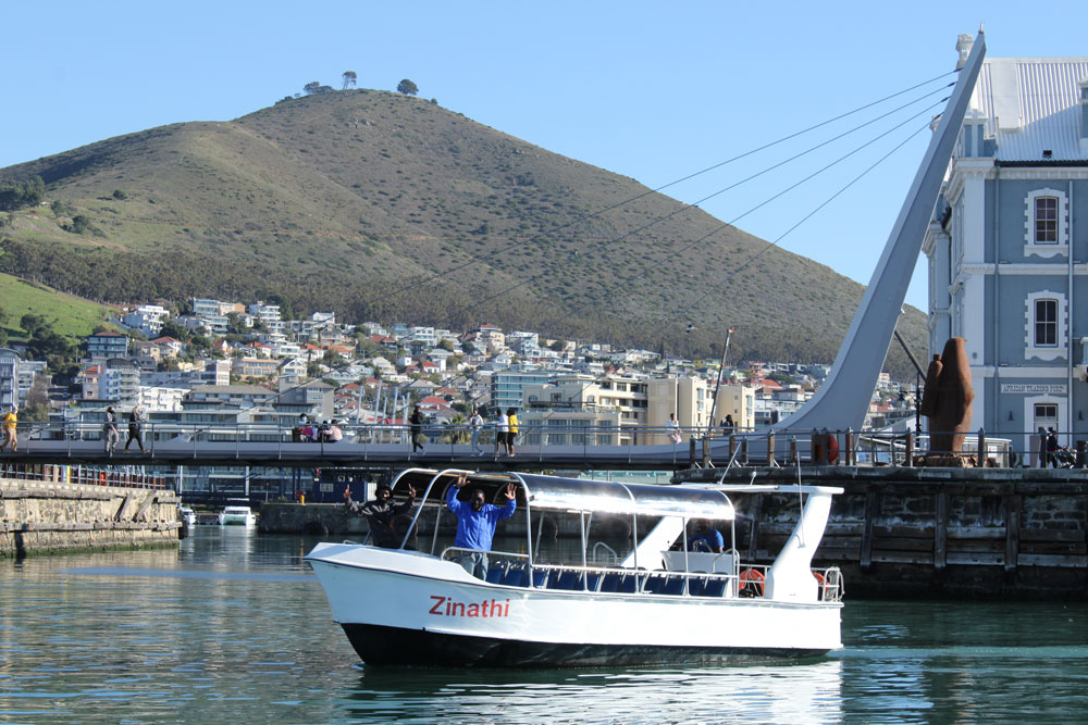 Boat on water with hillside and buildings in the background.