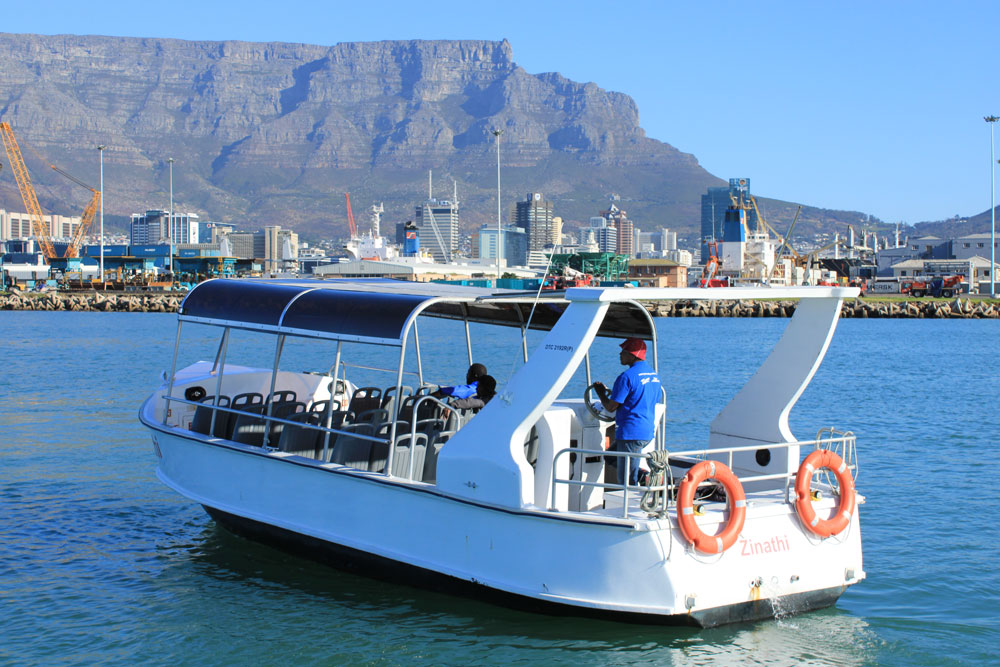 Boat with passengers on water, city and mountain backdrop.