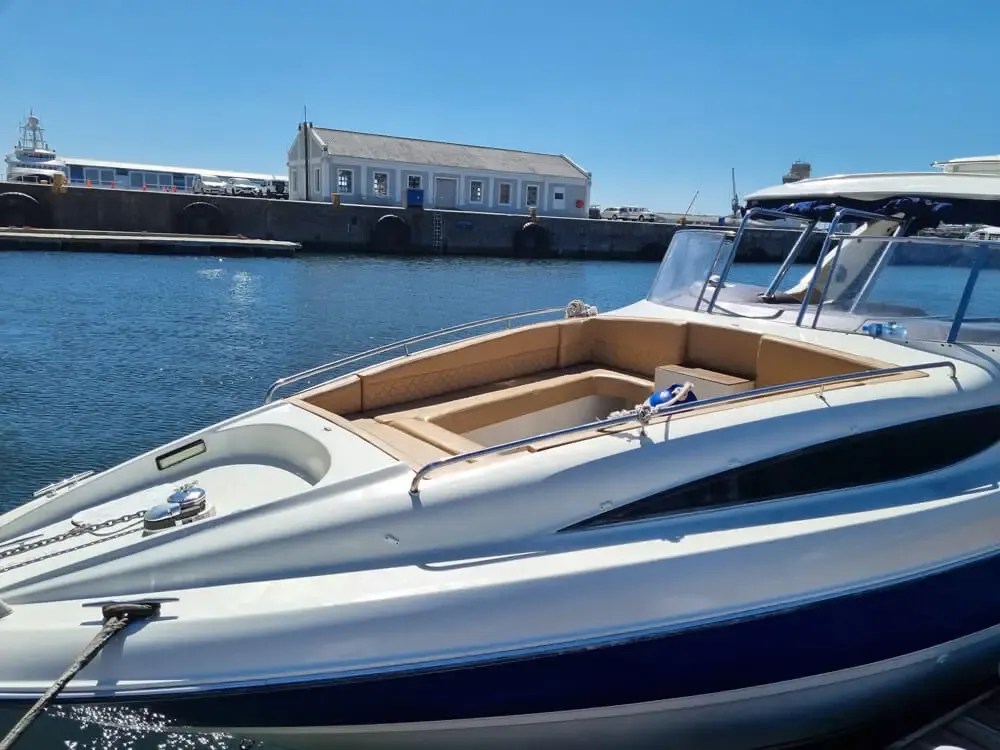 White motorboat docked in calm water near a pier building on a sunny day.