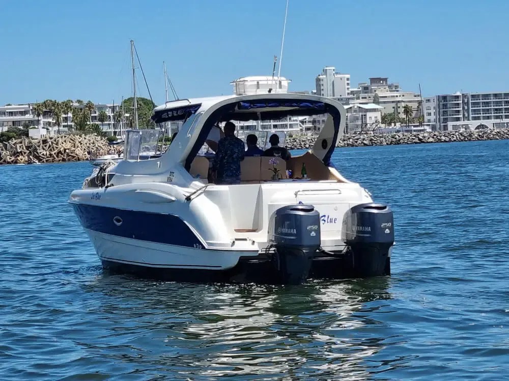 White boat with two engines on water, city skyline in background.